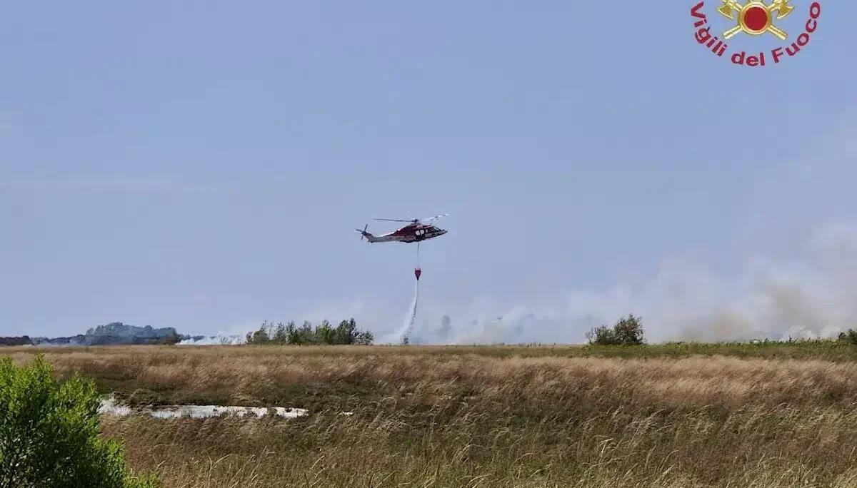 Incendio di sterpaglie su un isolotto in laguna: elicottero con benna in volo per spegnere il rogo - 
